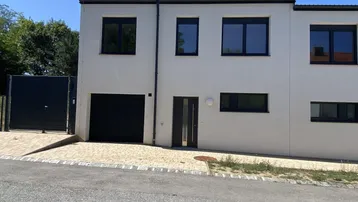 Moderne Reihenhausfassade mit dunklen Fenstern, integrierter Garage und Zufahrt.
