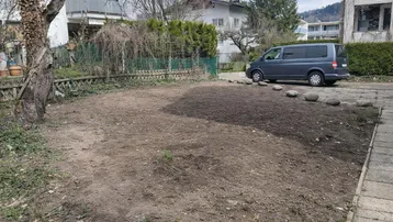 Vorbereiteter Gartenbereich mit einem geparkten Fahrzeug und umgebenden Bäumen sowie Hecken.