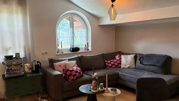 Gemütliches Wohnzimmer mit großem Ecksofa, stilvollen Beistelltischen und einem charmanten Rundbogenfenster.