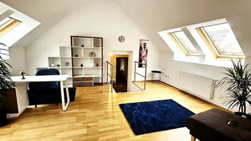 Heller Dachgeschoss-Wohnbereich mit Schreibtisch, Regalen und viel Tageslicht durch Dachfenster.