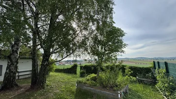 Grüner Gartenbereich mit Hochbeet, Bäumen und weitem Blick über die ländliche Landschaft.