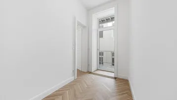 Lichtdurchfluteter Flur mit Fischgrätparkett und einem französischen Balkon am Ende.