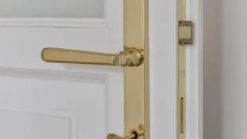 Detailaufnahme einer weißen Tür mit elegantem goldenem Türgriff und Schlüssel im Schloss.