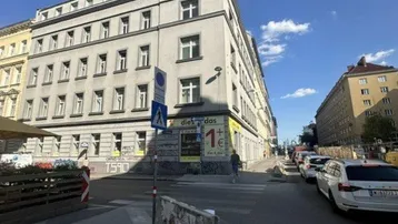 Gebäudeansicht von der Straßenecke mit geparkten Autos und blauem Himmel.