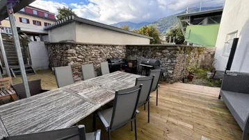 Geräumige Holzterrasse mit großem Esstisch, Grillbereich und malerischem Bergblick.