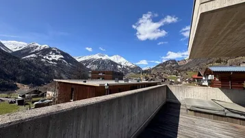 Panoramablick von der Terrasse auf die schneebedeckten Berge und die umliegende Siedlung unter blauem Himmel.