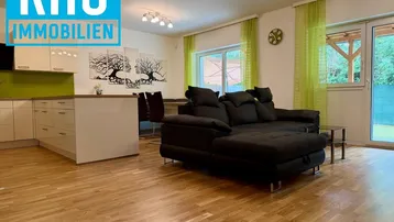Offener Wohn-Essbereich mit moderner Küche, Sofa und Zugang zur Terrasse.