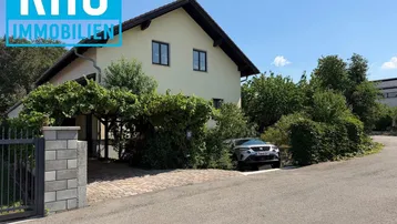 Einfamilienhaus mit heller Fassade, Satteldach und gepflegter Einfahrt unter blauem Himmel.