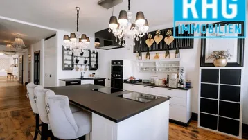 Moderne offene Küche mit Kochinsel, dunklen Arbeitsplatten und Holzboden, beleuchtet von eleganten Kronleuchtern.