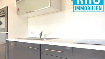 Moderne Küche mit grauen Hochglanzfronten, Spüle, Induktionskochfeld und integriertem Backofen.
