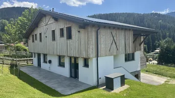 Modernes Chalet mit Holzfassade, großer Terrasse und Photovoltaikanlage in alpiner Umgebung.
