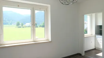 Heller Wohnbereich mit großem Fenster, Blick ins Grüne und Zugang zur Küche.