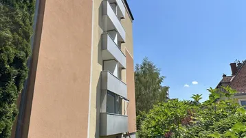 Seitenansicht eines Wohngebäudes mit mehreren Balkonen und üppigem Grün.