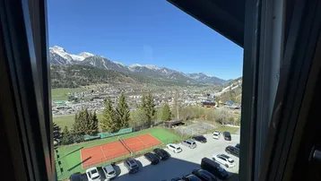 Ausblick aus dem Fenster auf schneebedeckte Berge, einen Tennisplatz und die umliegende Landschaft.