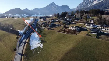 Luftaufnahme einer ländlichen Gegend mit Häusern, Feldern und schneebedeckten Bergen im Hintergrund.