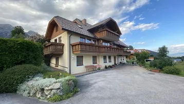 Charmantes Gebäude mit Holzbalkonen und gepflegtem Vorgarten unter einem bewölkten Himmel.