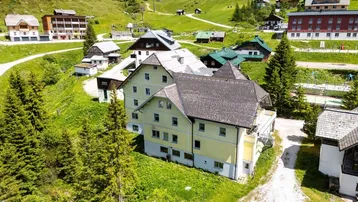 Luftaufnahme eines Gebäudekomplexes in einer grünen Berglandschaft mit umliegenden Häusern.