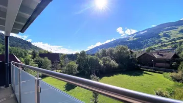 Sonniger Balkon mit Glasgeländer und herrlichem Blick auf die grüne Berglandschaft.