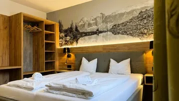 Geräumiges Schlafzimmer mit Doppelbett, offenem Kleiderschrank und Wandbild mit Bergsee.