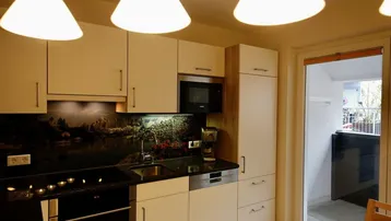 Moderne Küche mit weißen Schränken, schwarzer Arbeitsplatte und Zugang zu einem Balkon.