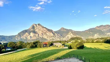 Malerischer Ausblick auf die Berglandschaft und den See im warmen Licht der Abendsonne, umgeben von weiten Feldern.