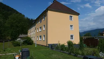Mehrfamilienhaus mit gepflegtem Gartenbereich und Blick auf die umliegende grüne Landschaft.
