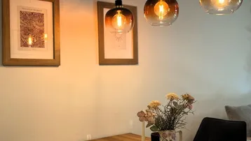 Nahaufnahme eines Esstisches mit dekorativen Pendelleuchten und gerahmten Bildern an der Wand.