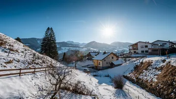 Sonnige Winterlandschaft mit Häusern und Bergen im Hintergrund, weite Aussicht.