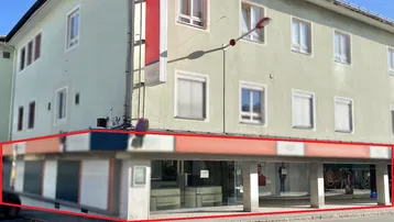 Außenansicht des Gebäudes mit der markierten Gewerbefläche im Erdgeschoss und großen Schaufenstern.
