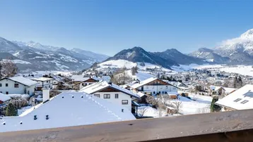 Weitläufiger Panoramablick vom Balkon über die verschneite Berglandschaft und das Dorf.