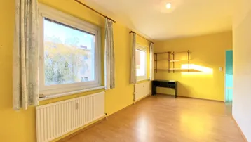 Helles Zimmer mit gelben Wänden, Holzoptikboden und Blick ins Grüne.