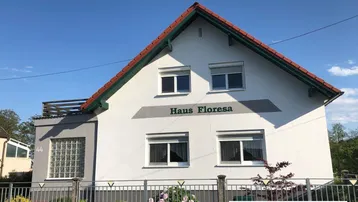Vorderansicht des Hauses mit weißer Fassade, Satteldach und einem blühenden Rosenbusch im Vorgarten.