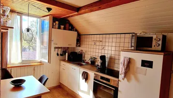 Helle Küche im Dachgeschoss mit Holzboden, weißen Schränken und Essbereich.