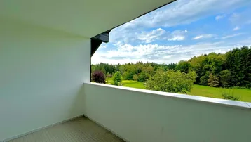 Balkon mit weitem Blick über grüne Wiesen und dichte Wälder unter blauem Himmel.
