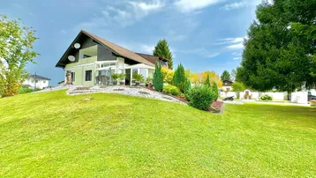 Großzügiger Gartenbereich mit gepflegtem Rasen und einem Einfamilienhaus auf einem Hügel.