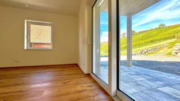 Heller Raum mit Holzboden, großen Glasschiebetüren und Blick auf die Weinberge.