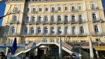 Gelbe Fassade eines historischen Gebäudes mit vielen Fenstern und Balkonen, beleuchtet von der Sonne.