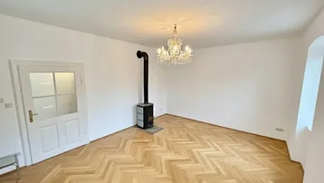 Helles Zimmer mit Fischgrätparkett und einem eleganten Kaminofen, ideal für gemütliche Abende.