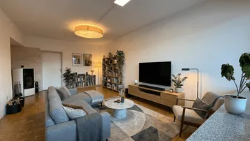Geräumiges Wohnzimmer mit gemütlicher Sitzecke, Fernseher und einem modernen Kaminofen.