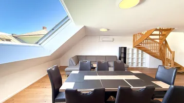 Geräumiger Wohn- und Essbereich mit Holzboden, Dachfenster und offener Holztreppe.