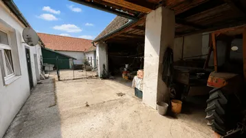 Blick vom überdachten Bereich in den sonnigen Innenhof mit alten Gebäuden und Holzbalken.