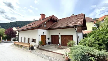 Charmantes Einfamilienhaus mit zwei Garagen und traditionellem Satteldach in grüner Umgebung.