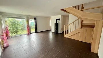 Geräumiges Wohnzimmer mit dunklen Fliesen, Holztreppe und einem modernen Kaminofen.