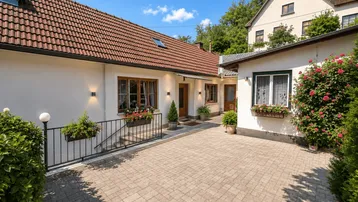 Außenansicht eines Hauses mit gepflastertem Hof und Blumenkästen unter den Fenstern.