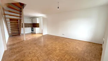 Heller offener Wohnbereich mit Parkettboden und integrierter Küche, verbunden durch eine Holztreppe.