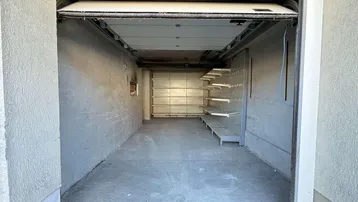 Leere Garage mit Betonboden und praktischen Regalsystemen an der Wand.