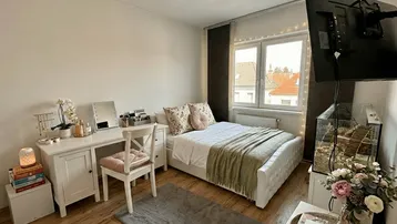 Helles Schlafzimmer mit Holzboden, Schminktisch und einem Fenster mit Blick ins Grüne.