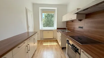 Helle Küche mit Holzoptik-Arbeitsplatten, Einbaugeräten und Fenster mit Blick ins Grüne.