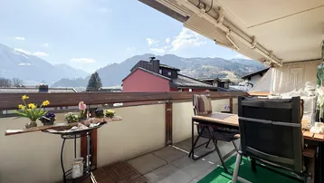 Geräumiger Balkon mit Holzbodenfliesen, Sitzgelegenheiten und einem weiten Blick auf die umliegende Berglandschaft.