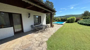 Große gepflasterte Terrasse mit Esstisch und Blick auf den Pool und die umliegende Landschaft.